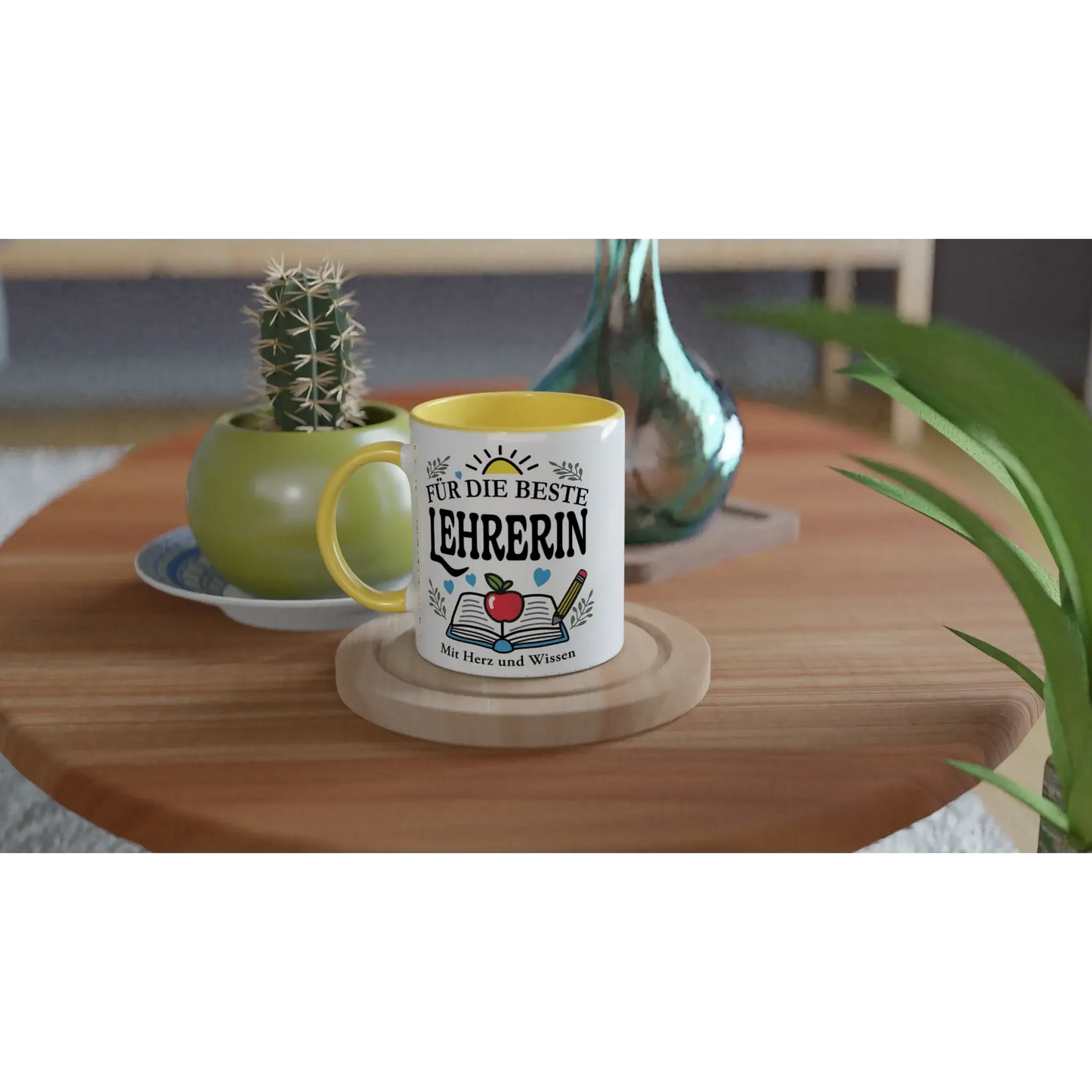 Gift the beste Lehrerin a Tasse âFĂŒr die beste Lehrerinâ from Tasse mit Herz, featuring an apple and books. It rests on a wooden table with a cactus and glass decor amid green leaves.
