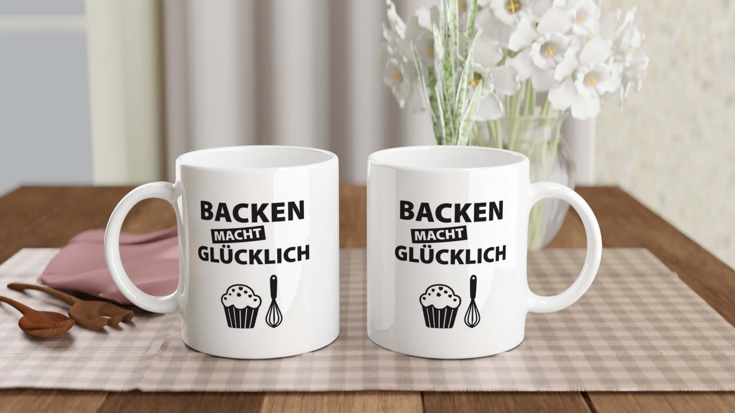 Zwei "Backen macht glĂźcklich"-Tassen nebeneinander auf gedecktem Tisch