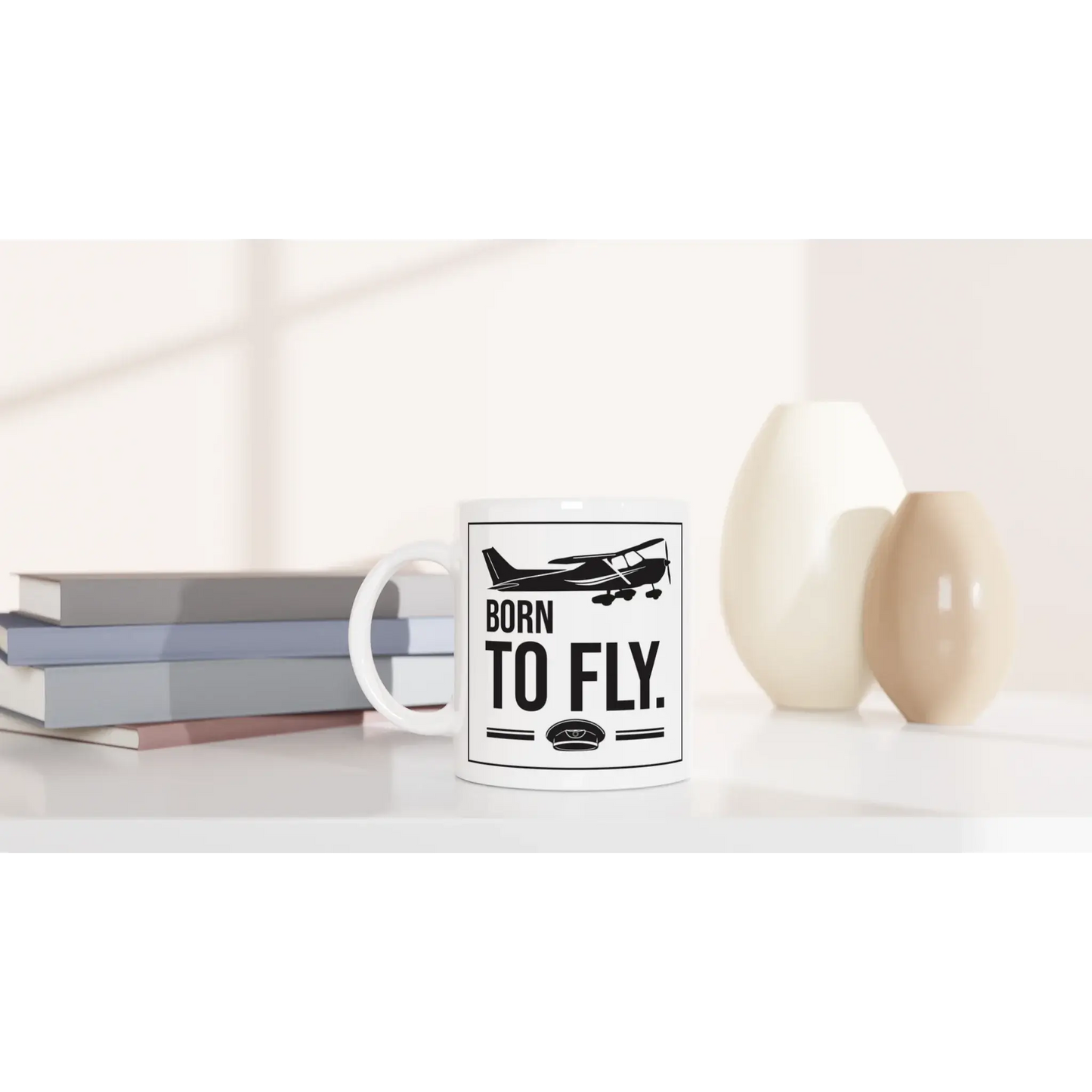 Tasse "Born to fly" neben Bücherstapel und Vasen, ideal für Piloten und Flugbegeisterte.