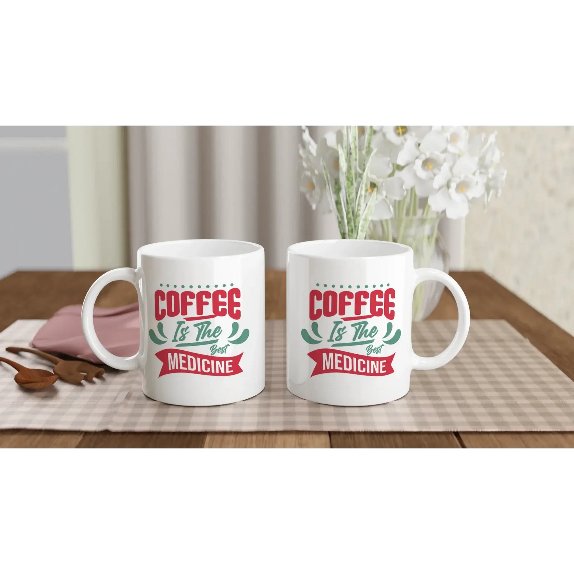 Zwei weiße Tassen auf einer karierten Tischdecke zeigen „Kaffee ist die beste Medizin“ – ideal für Kaffeefans mit Humor von Tasse mit Herz. Das Arrangement besteht aus einem Strauß weißer Blumen, Holzbesteck und einem rosafarbenen Gegenstand daneben.