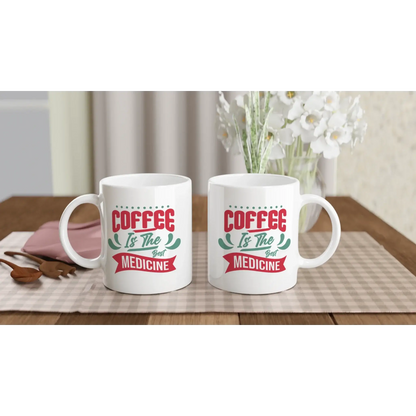 Zwei weiße Tassen auf einer karierten Tischdecke zeigen „Kaffee ist die beste Medizin“ – ideal für Kaffeefans mit Humor von Tasse mit Herz. Das Arrangement besteht aus einem Strauß weißer Blumen, Holzbesteck und einem rosafarbenen Gegenstand daneben.