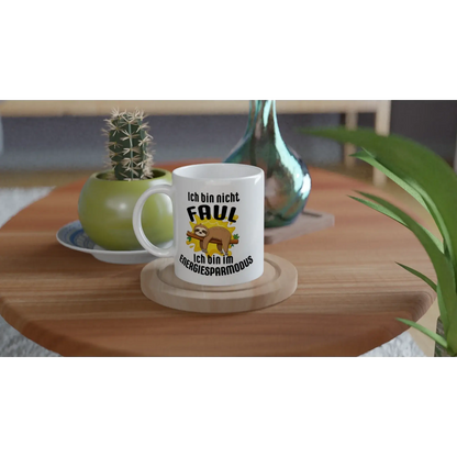 Eine Tasse mit Herz's Humorvoller Kaffeebecher „Ich bin nicht faul“ ziert den Holztisch und hebt ein Cartoon-Faultier mit „Ich bin nicht faul, ich bin im Energiesparmodus“ hervor. In der Nähe vervollständigen eine grüne Vase und ein kleiner Kaktus diese bezaubernde Szene – ideal für einen entspannten Lebensstil.