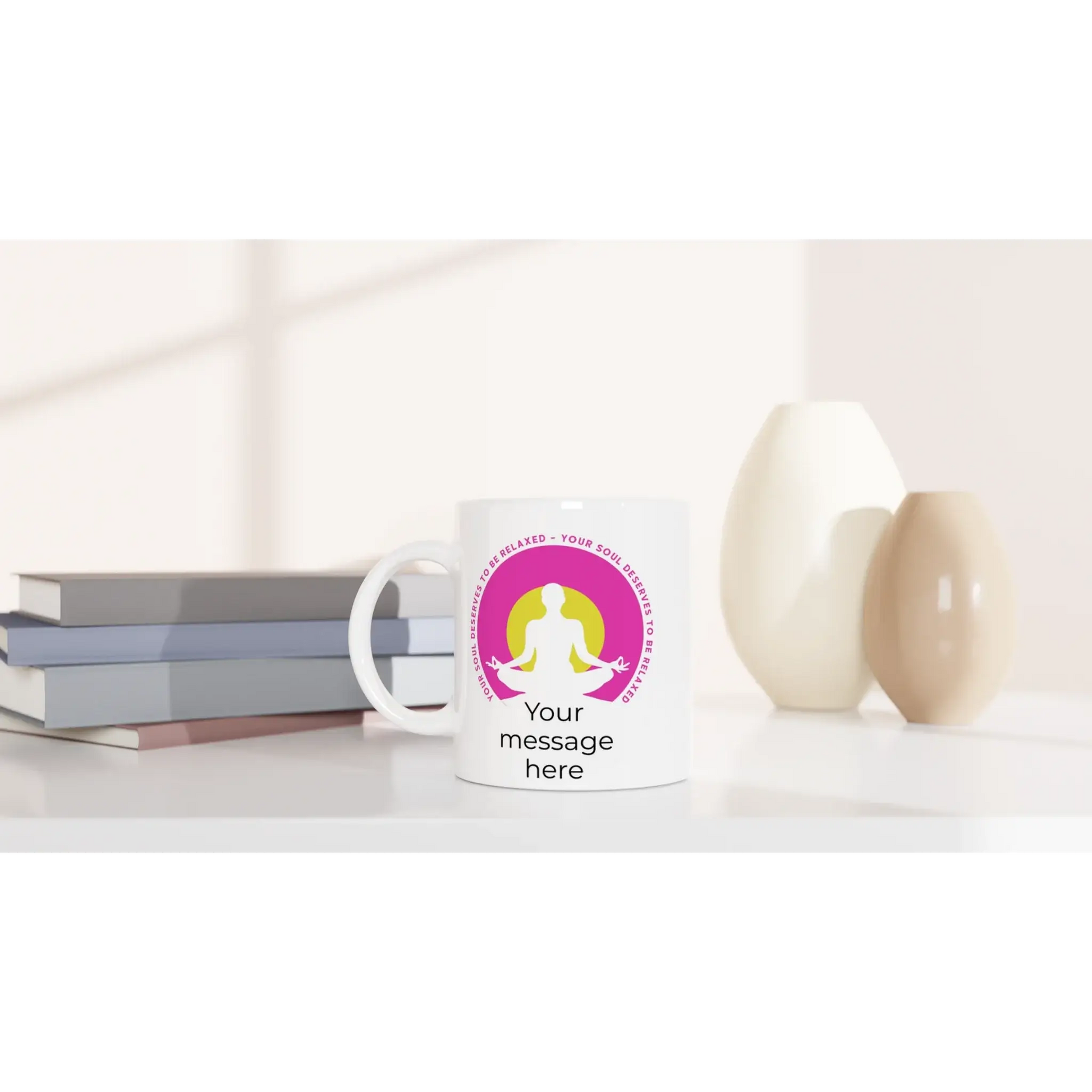 Eine weiße Tasse mit dem Titel „Yoga Tasse ‚Deine Seele verdient Entspannung‘“ von Tasse mit Herz steht auf einem Tisch. Ein rosa-gelbes Meditationslogo symbolisiert Achtsamkeit und Harmonie. Darunter steht „Deine Nachricht hier“. Daneben sind gestapelte Bücher und zwei dekorative Vasen zu sehen.
