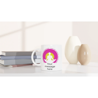 Eine weiße Tasse mit dem Titel „Yoga Tasse ‚Deine Seele verdient Entspannung‘“ von Tasse mit Herz steht auf einem Tisch. Ein rosa-gelbes Meditationslogo symbolisiert Achtsamkeit und Harmonie. Darunter steht „Deine Nachricht hier“. Daneben sind gestapelte Bücher und zwei dekorative Vasen zu sehen.