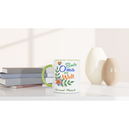 A Tasse mit Herz, featuring Beste Oma der Welt and customizable text, adorned with floral designs, is the perfect personalisierbares Geschenk for your Großmutter. It sits elegantly on a table among books and ceramic vases in soft lighting.