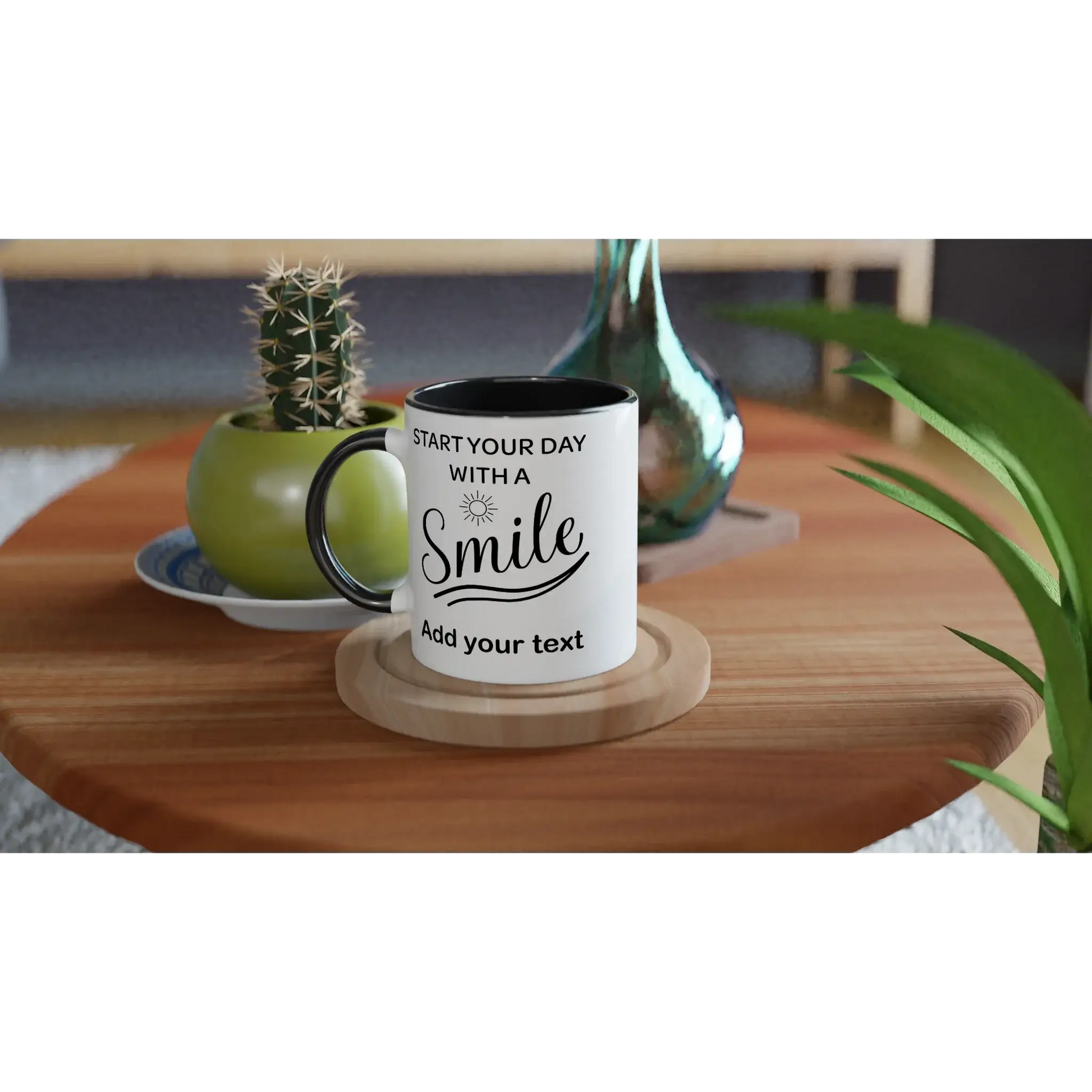 Personalisierbare Tasse mit Spruch "Start your day with a smile" auf einem Tisch mit Pflanzen.