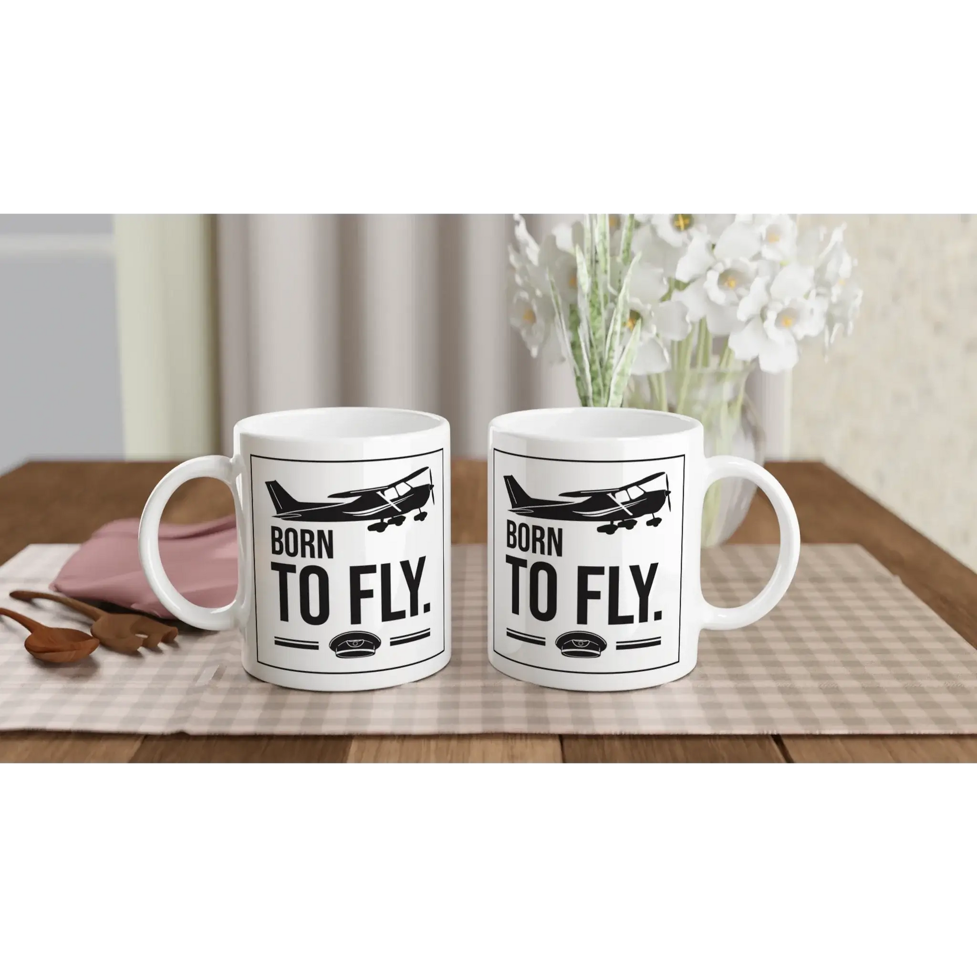 Tassen mit dem Aufdruck „Born to fly“ für Piloten und Flugbegeisterte auf einem Holztisch.