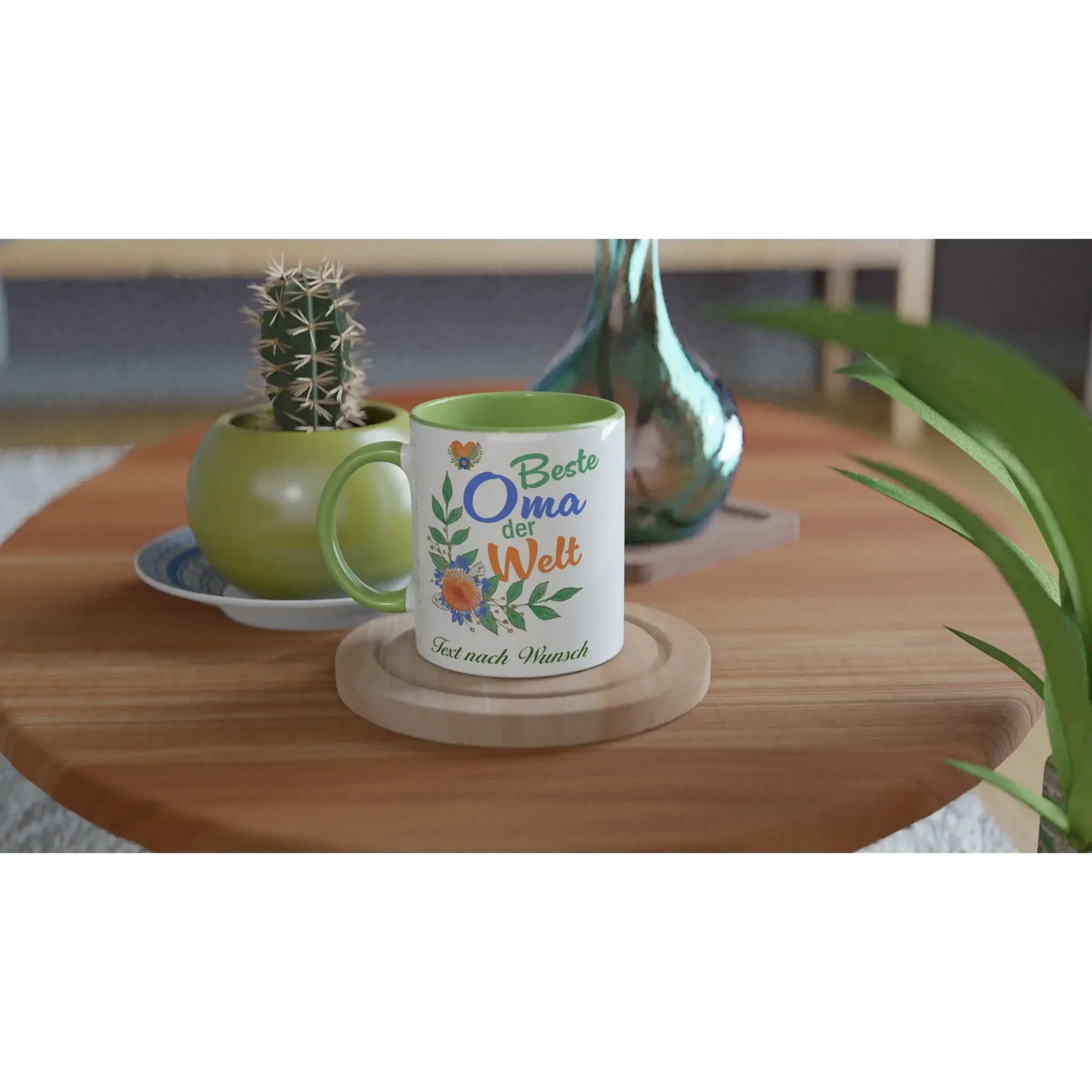 On a wooden table, the Tasse mit Herz features the Tasse Beste Oma der Welt, adorned with flowers and a butterfly, ideal as a personalisierbares Geschenk for your Großmutter. Its placed next to a cactus in a green pot and a metallic vase.