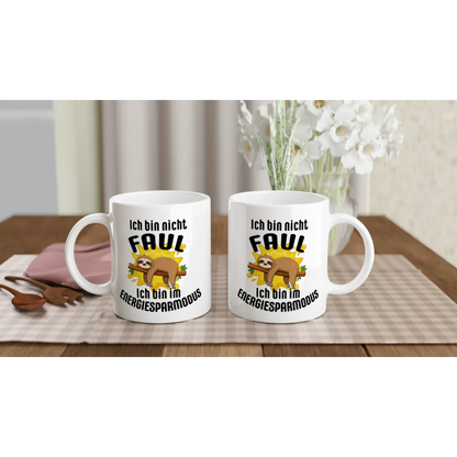 Zwei weiße Tassen von Tasse mit Herz auf einer karierten Tischdecke. Jede Tasse zeigt ein Cartoon-Faultier und den deutschen Text „Ich bin nicht faul. Ich bin im Energiesparmodus“. Passend zum Strauß weißer Blumen und Utensilien im Hintergrund. Perfekt als ☕️ Humorvoller Kaffeebecher für entspannte Momente! 😴.