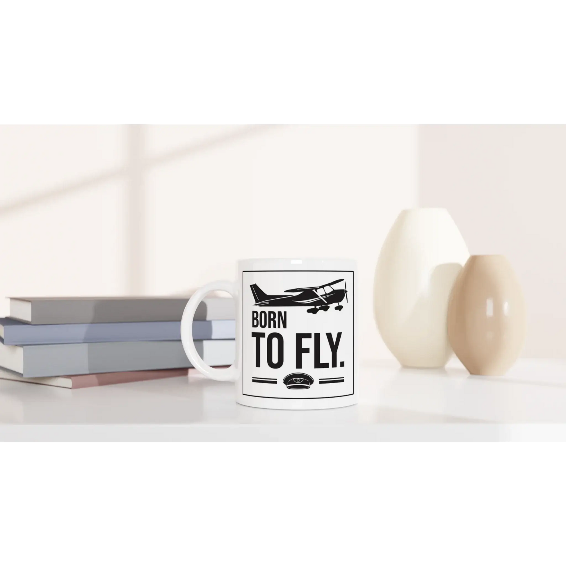 Tasse "Born to fly" neben Bücherstapel und Vasen, ideal für Piloten und Flugbegeisterte.